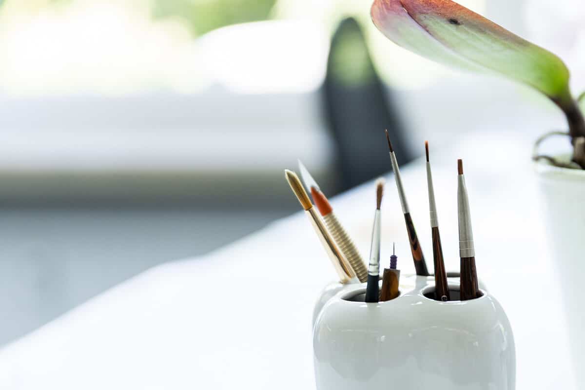 Mehrere Pinsel und Stifte in einem weißen Gefäß auf hellem Untergrund.