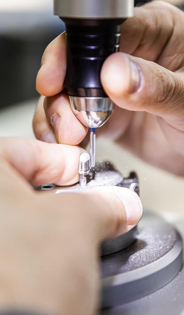 Nahaufnahme von Händen, die mit einem Schleifgerät an einem kleinen Zahn arbeiten.