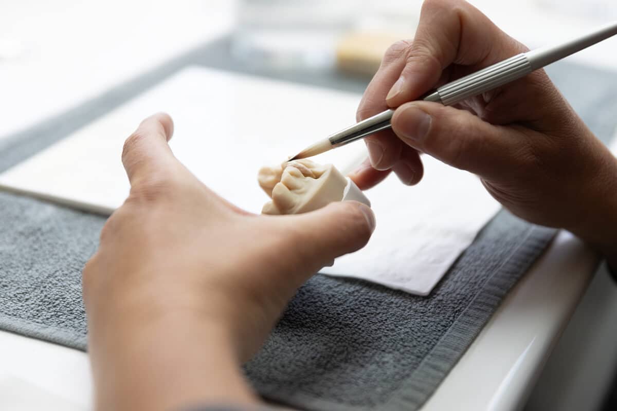 Hände bemalen mit einem Pinsel einen Zahnersatz.