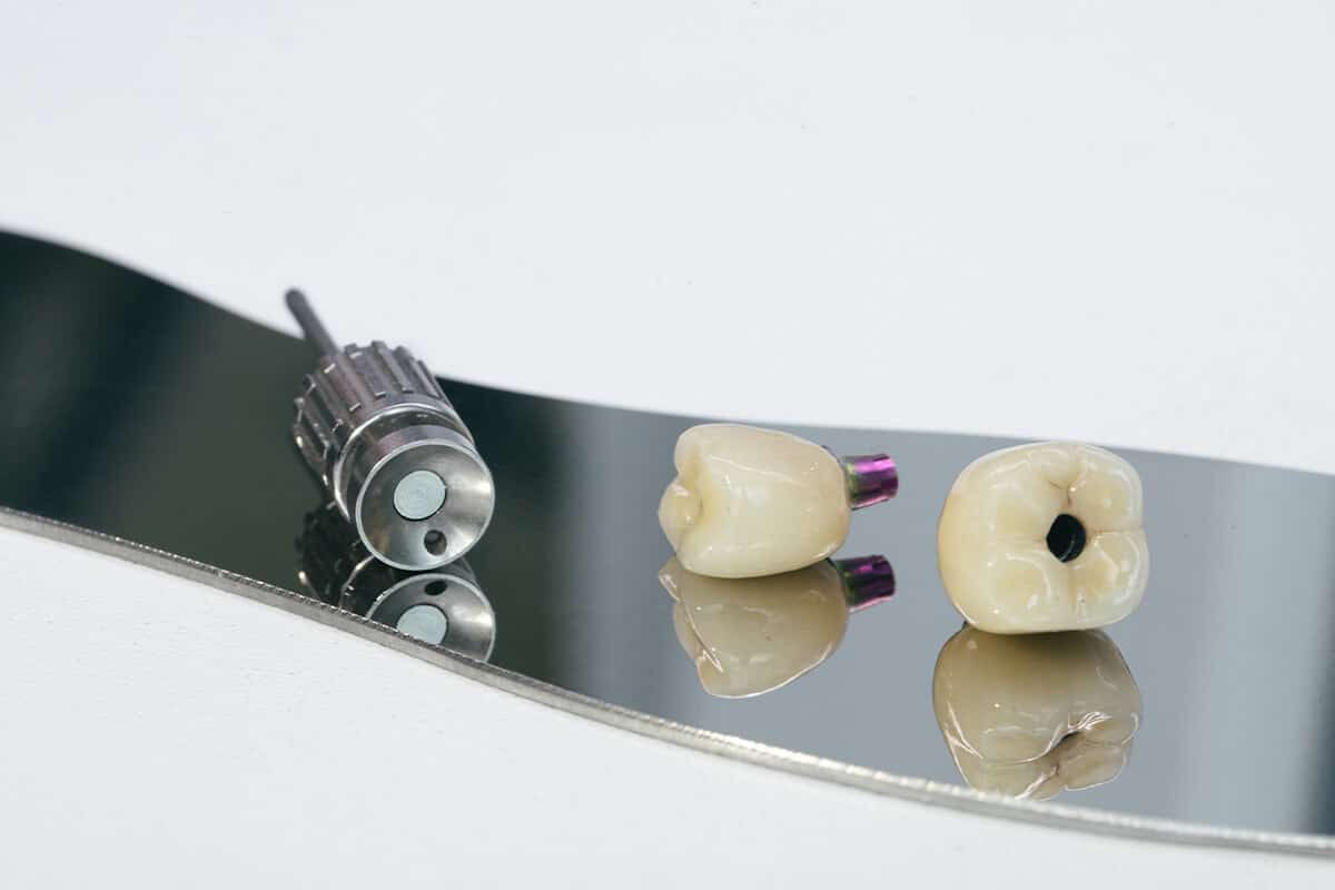 Zwei individuelle Zahnabutments und ein zylindrisches Metallinstrument liegen auf einer reflektierenden Oberfläche.