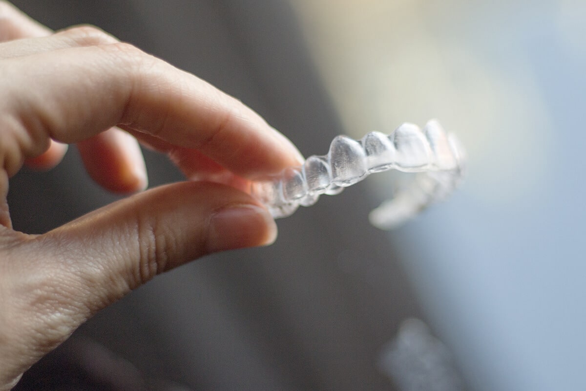 Hand hält eine transparente Zahnschiene aus Kunststoff zwischen Daumen und Zeigefinger.