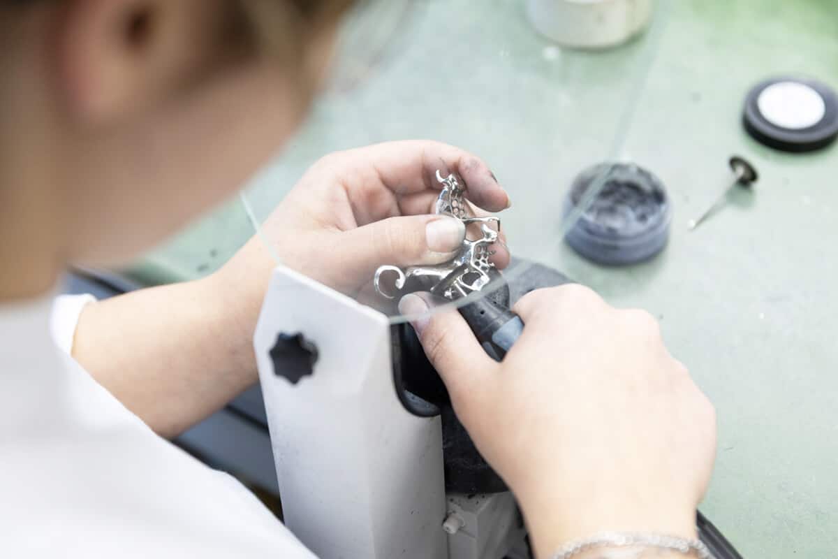 Zahntechnikerin bearbeitet ein filigranes Metallgerüst für eine Teilprothese mit einem rotierenden Werkzeug.