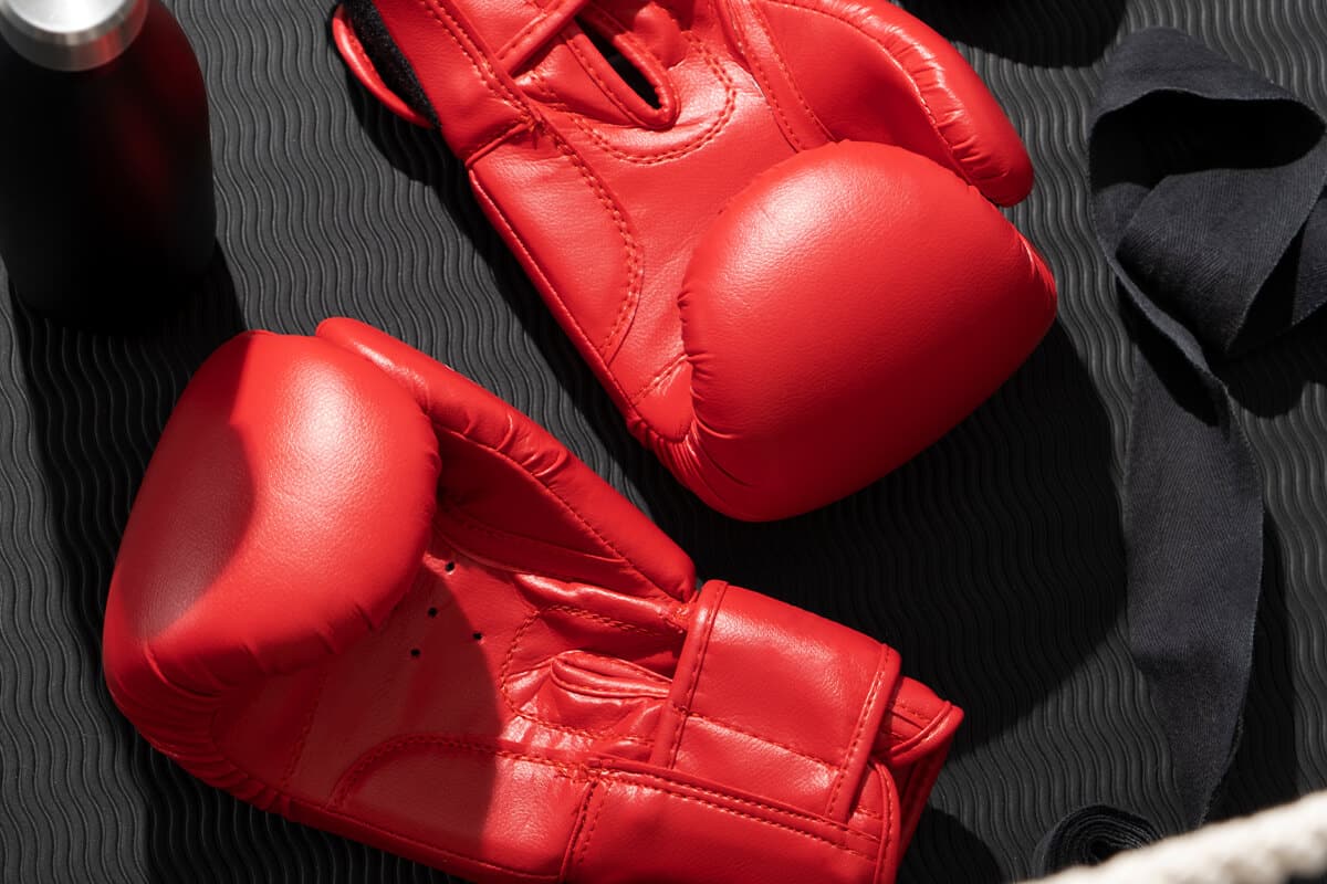 Zwei rote Boxhandschuhe liegen auf einer schwarzen, geriffelten Oberfläche.