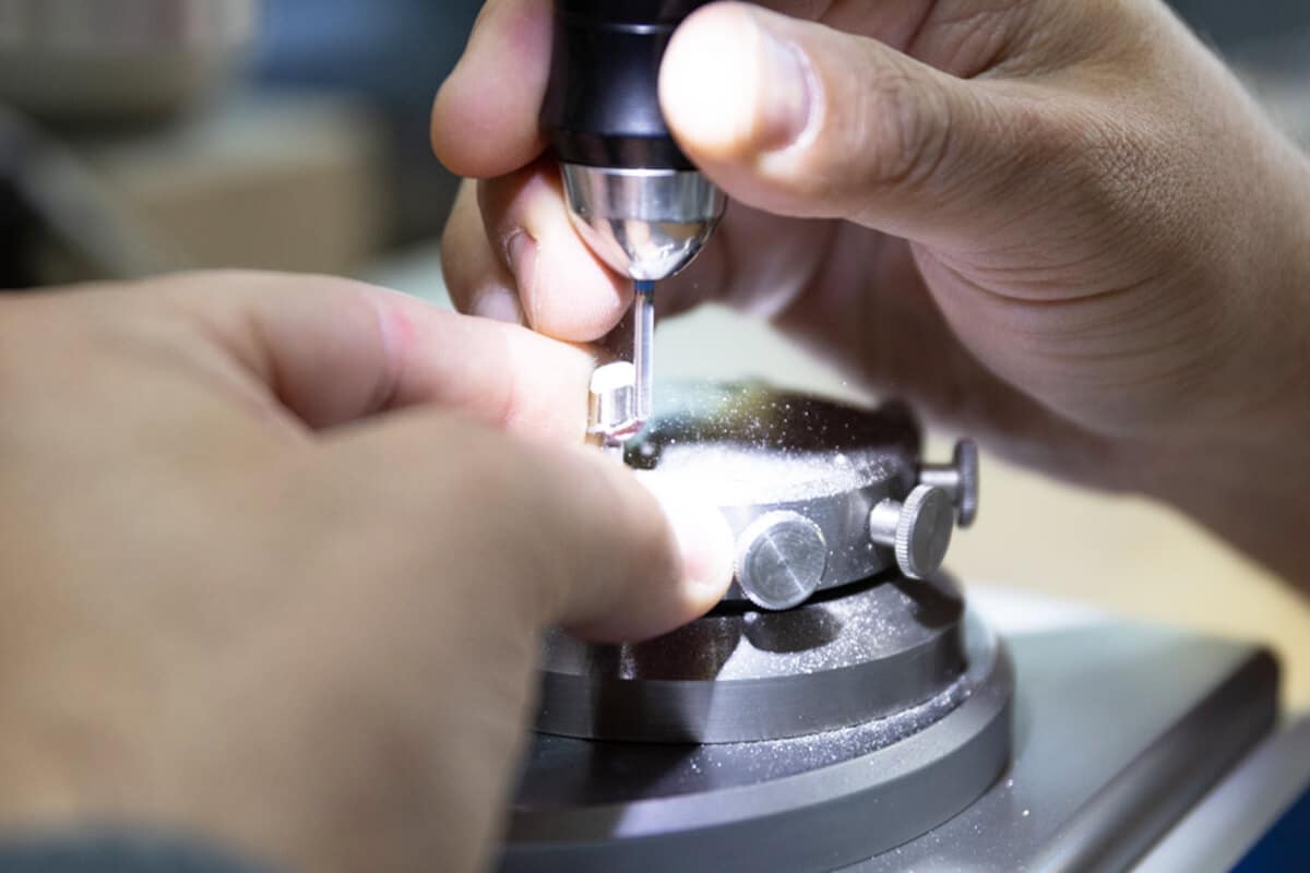 Nahaufnahme von Händen, die mit einem Schleifgerät an einem kleinen Zahn arbeiten.
