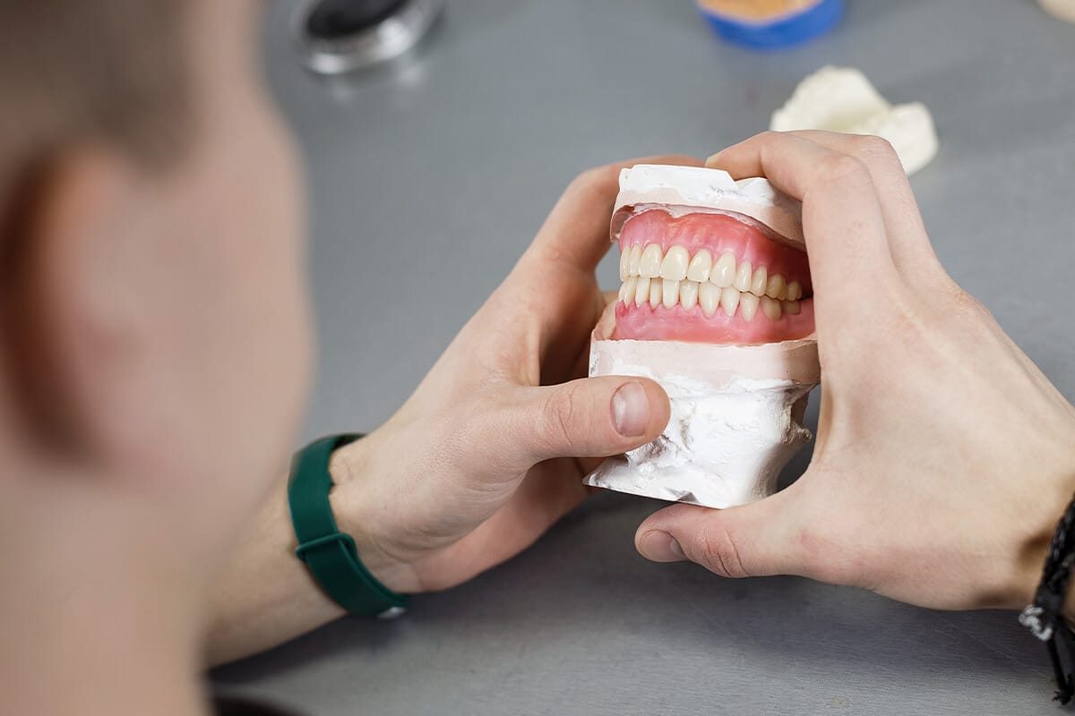 Person hält ein Modell einer Totalprothese mit sichtbaren Zähnen und Zahnfleisch in den Händen.