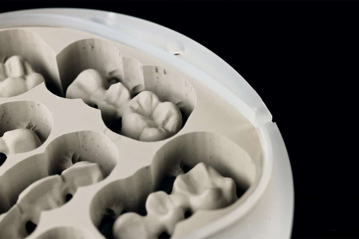 Nahaufnahme eines weißen Kunststoffbehälters mit mehreren Vertiefungen, die Zahnmodelle enthalten.